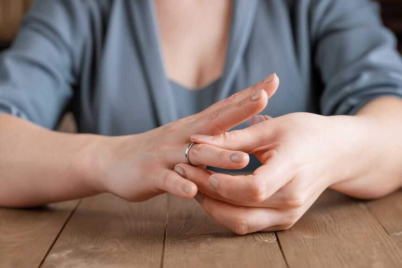 Женщина снимает кольцо с пальца обеими руками